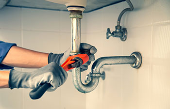 Technician plumber using a wrench to repair a water pipe under the sink