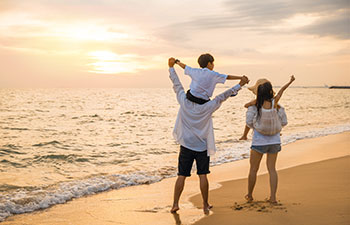 Parents carrying children on shoulders at the beach on sunset time