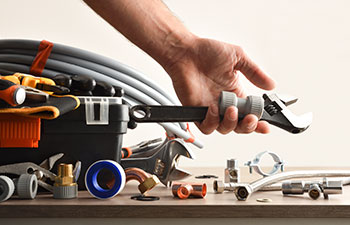 Plumber toolbox with material on wooden table and hand picking accessories with isolated background