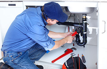 Mature plumber fixing a sink at kitchen