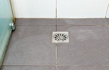 The hair loss clogs the metal drain cover on the black floor tiles in the shower room